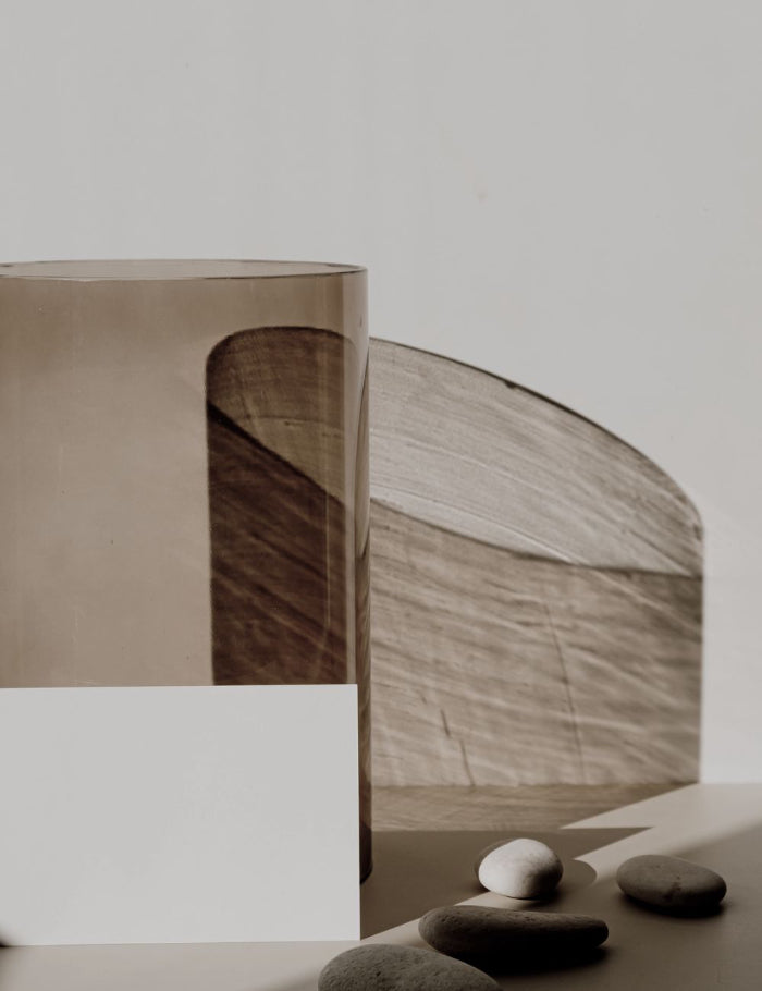 Two glass cylindrical shapes sit on a table with rocks overset by light and shadow.
