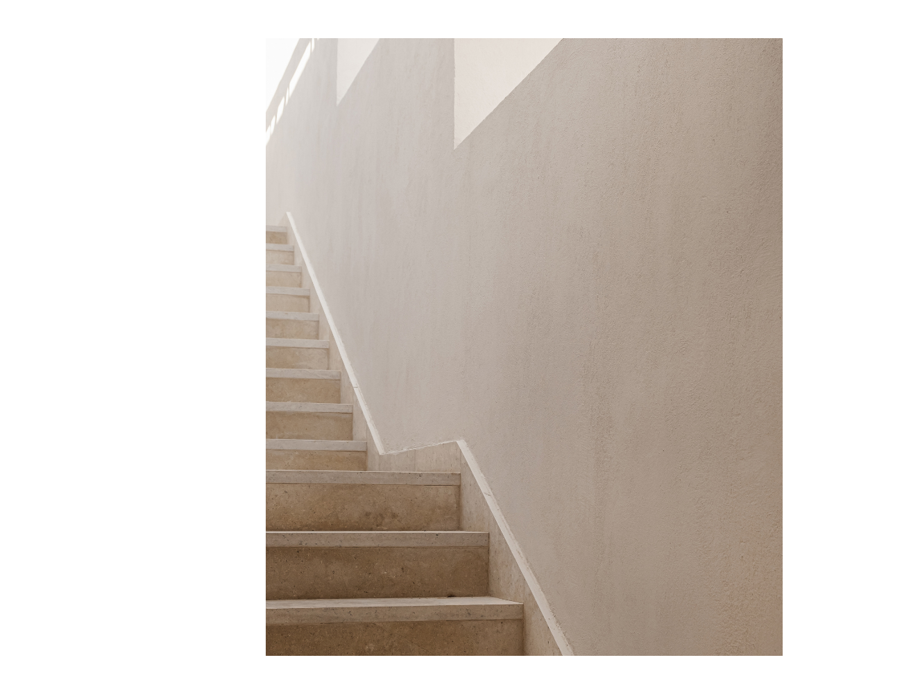 White stairs are ascending from shadow to light. Sunlight is just seen peeking through the windows.