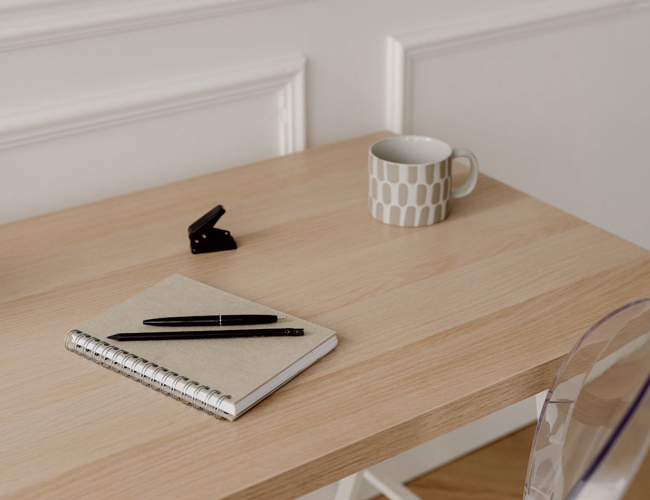 A notebook, pen, stapler and coffee mug are sitting on top of a wooden desk.